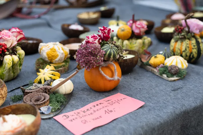 Dekorative Duftkerzen in kleinen Kürbissen und mit Blumen geschmückten Flaschenkürbissen auf einem Marktstand mit einem rosa Preisschild.