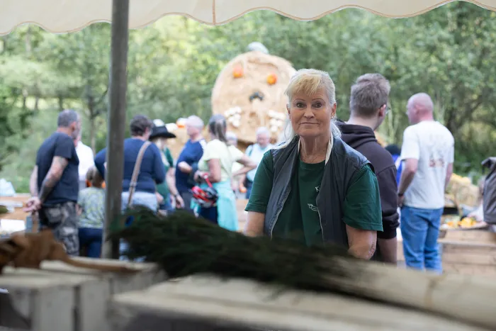 Eine blonde Frau blickt in die Kamera, im Hintergrund sind zahlreiche Besucher einer Veranstaltung im Freien zu sehen.