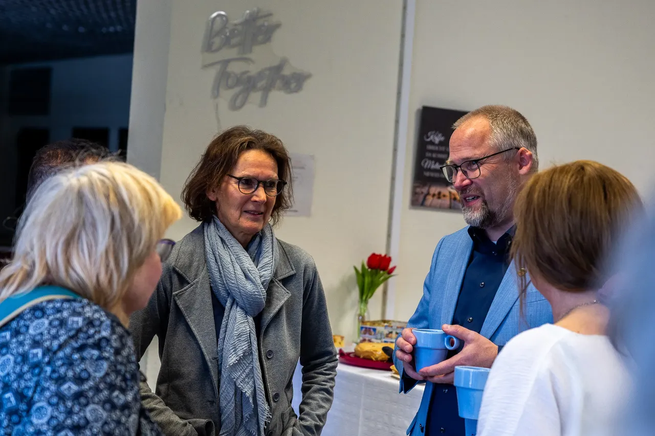 Zwei Frauen und ein Mann unterhalten sich auf einem Treffen im Jugendcafé Aquarium. Im Hintergrund steht ein Tisch mit Speisen und Getränken.