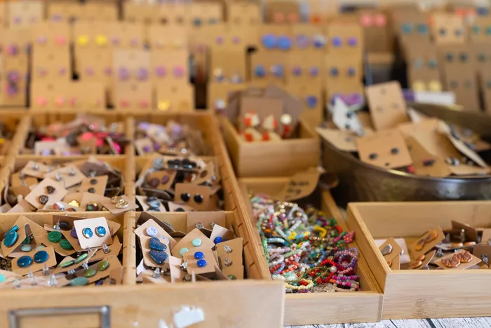 Verschiedene bunte Ohrringe in hölzernen Schalen und auf kleinen Karten auf einem Marktstand.