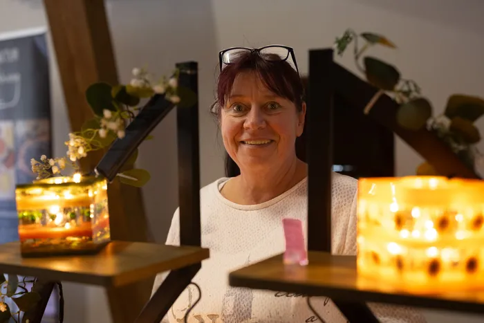 Eine lächelnde Frau mit Brille auf dem Kopf hinter zwei warm leuchtenden Dekolampen.