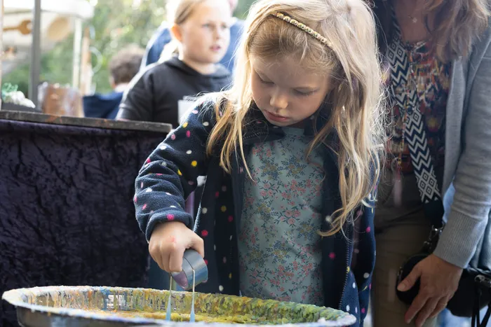 Ein kleines Mädchen arbeitet mit bunten Farben in einer flachen Schale bei einer Veranstaltung in der Heesfelder Mühle.