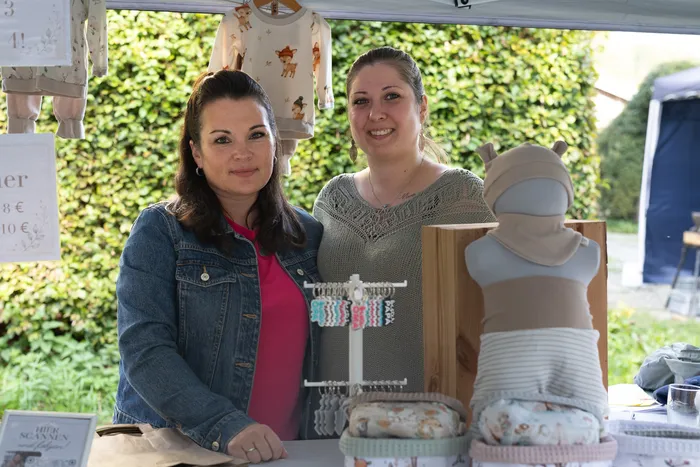Zwei Frauen stehen hinter einem Stand mit Babykleidung und Schmuck.