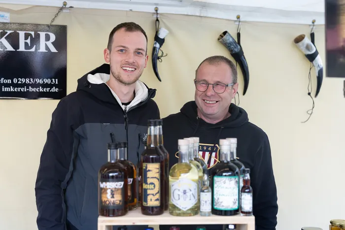 Zwei lächelnde Männer stehen hinter einem Stand mit verschiedenen Spirituosenflaschen wie Whiskey, Rum und Gin.