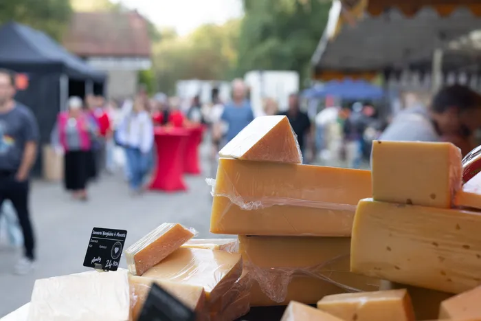 Große Stücke und Keile von gelbem Käse auf einem Marktstand vor einem unscharfen Hintergrund mit Marktbesuchern.
