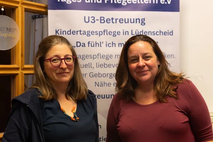 Zwei lächelnde Frauen stehen vor einem Banner für die U3-Betreuung und Kindertagespflege in Lüdenscheid.