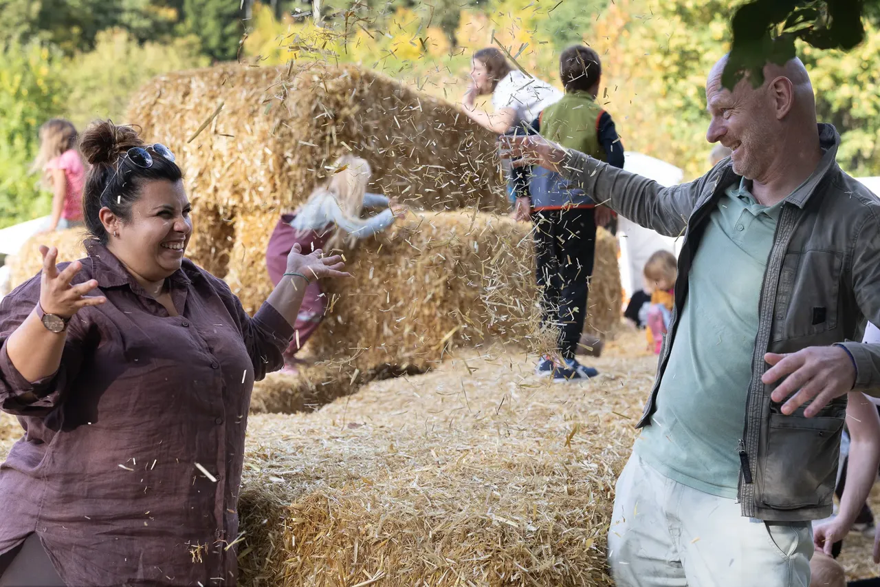 Eine Frau und ein Mann werfen Stroh in die Luft vor großen Strohballen.