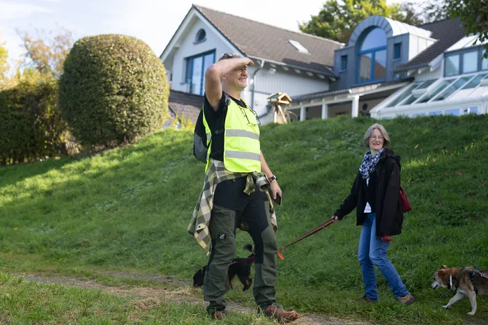 Ein Mann in einer gelben Warnweste und eine Frau gehen mit Hunden einen grasbewachsenen Hang entlang.