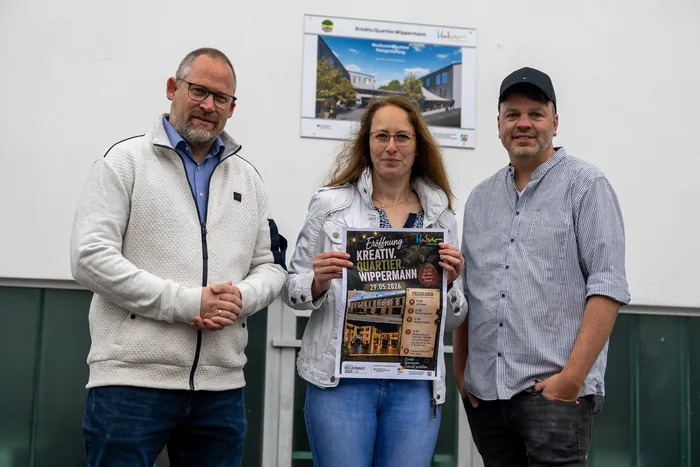 Bürgermeister Armin Kibbert, Yvonne Behnke und Matthias Clever halten ein Plakat für die Eröffnung des Kreativ.Quartier.Wippermann am 29. Mai im Denkhof Halver hoch.