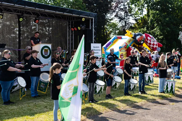 Musikzug des KKSV Meinerzhagen spielt auf dem Schützenplatz während des Jubiläumsfests. Im Hintergrund eine Hüpfburg und eine Bühne mit der Aufschrift „Herzlich Willkommen beim“.