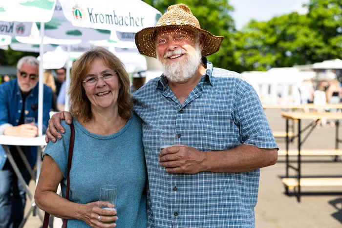 Lachendes Paar umarmt sich auf dem Schützenplatz während des Jubiläumsfests des KKSV Meinerzhagen. Im Hintergrund sind weitere Menschen und ein Krombacher-Schirm zu sehen.