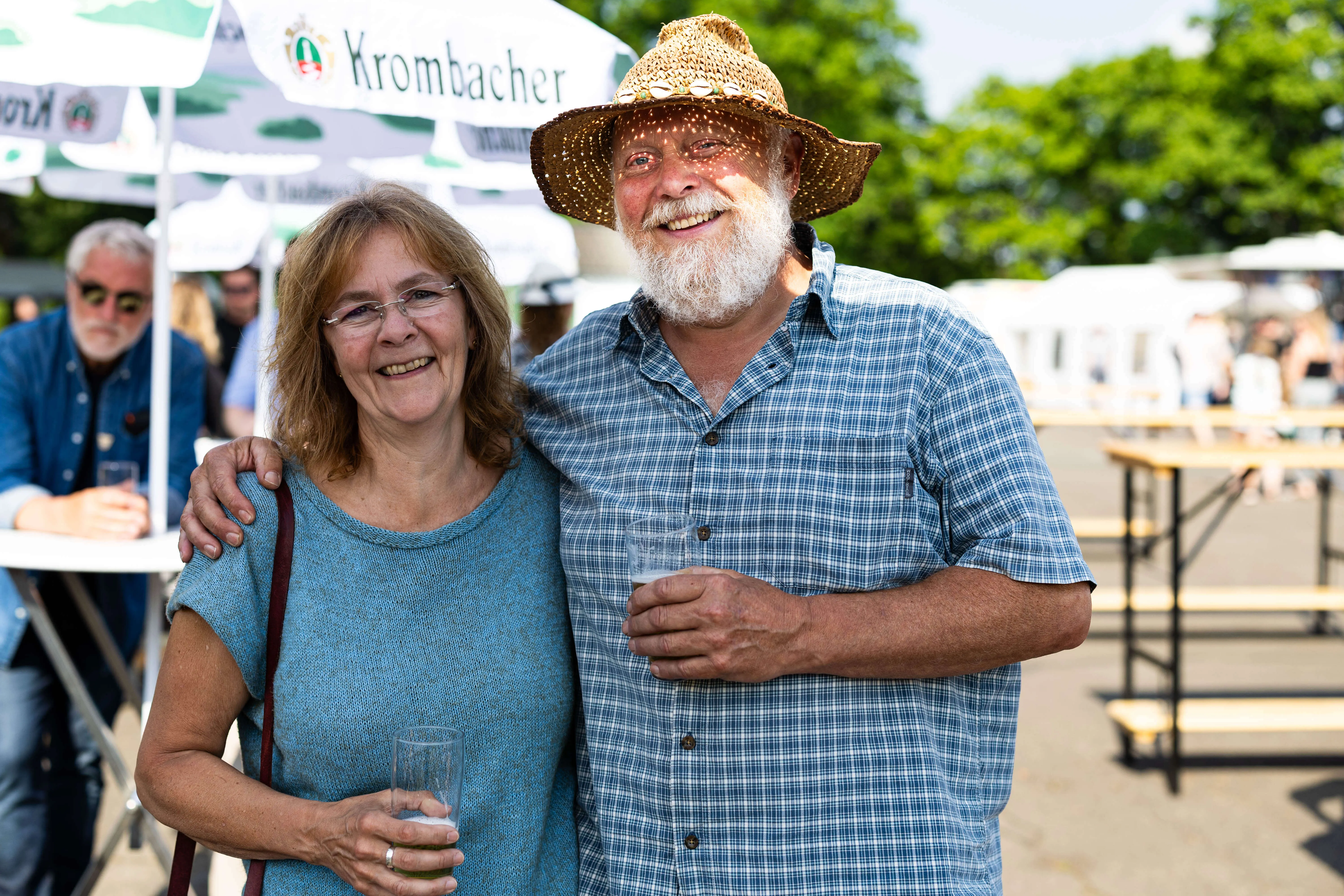 Lachendes Paar umarmt sich auf dem Schützenplatz während des Jubiläumsfests des KKSV Meinerzhagen. Im Hintergrund sind weitere Menschen und ein Krombacher-Schirm zu sehen.