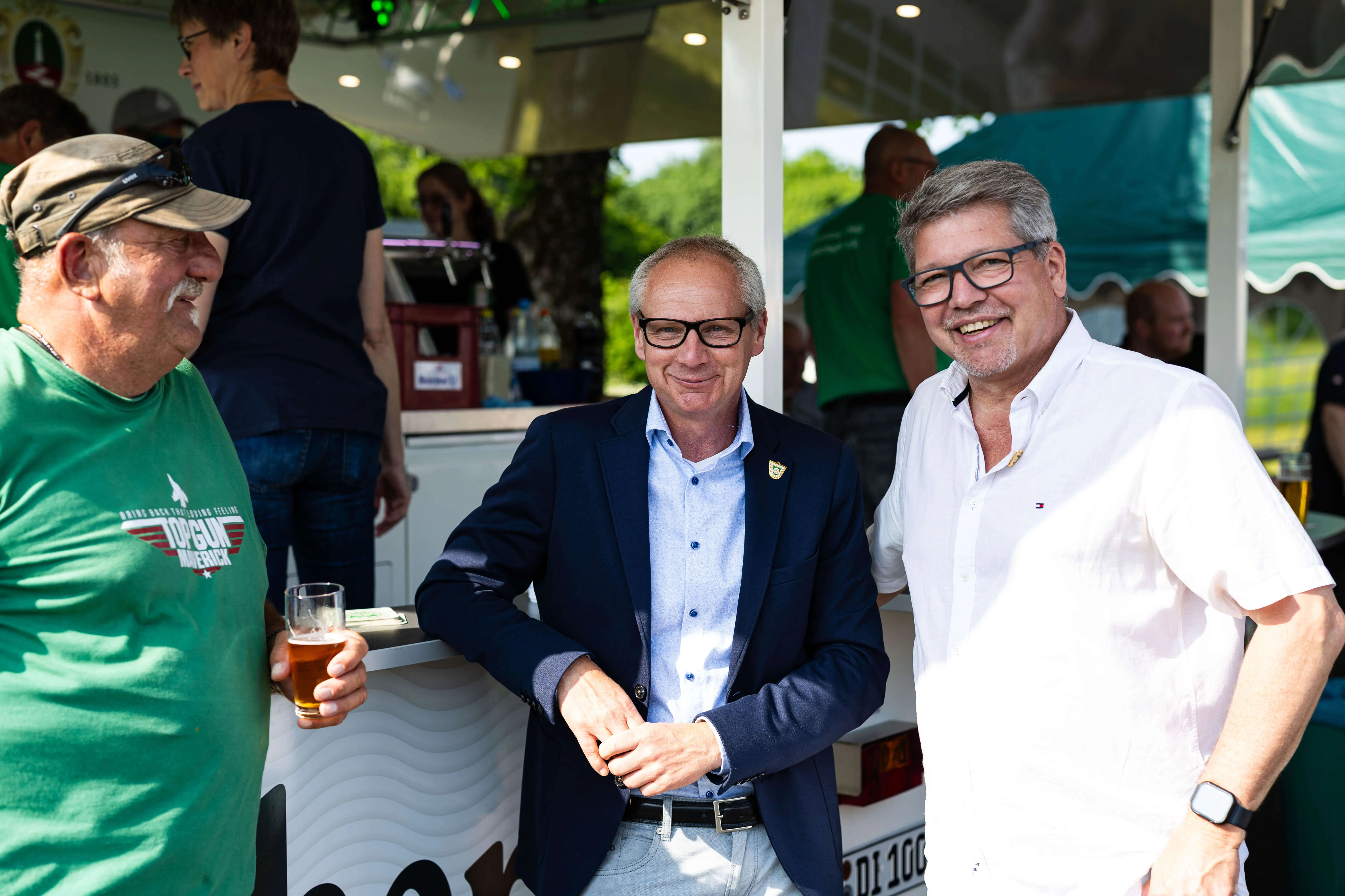 Drei Männer im Gespräch auf einem Fest, vermutlich zum 75-jährigen Jubiläum des KKSV Meinerzhagen. Der Mann in der Mitte trägt einen blauen Blazer und lächelt in die Kamera.