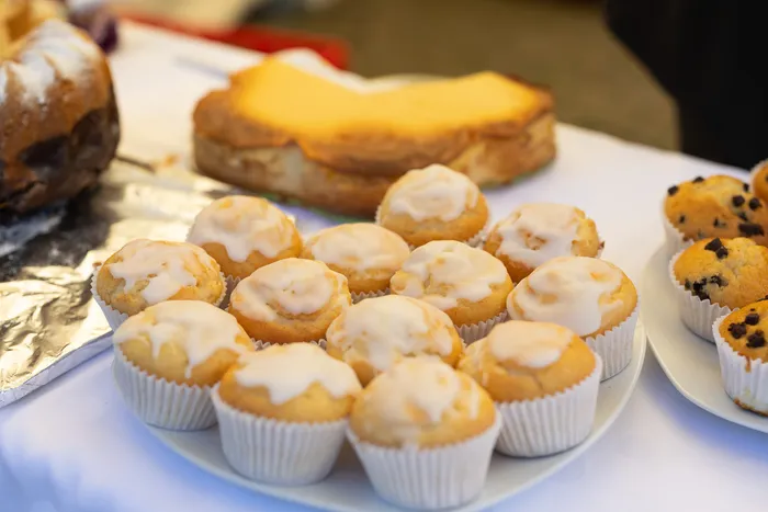 Verschiedene Kuchen und mit weißem Guss verzierte Muffins auf einem weiß gedeckten Tisch.