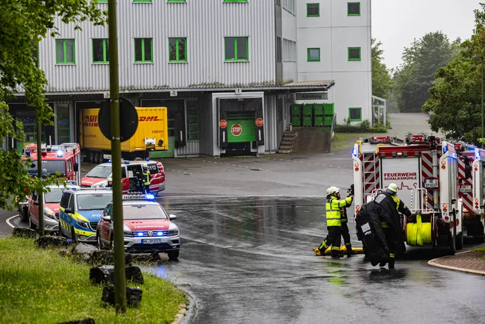Einsatzkräfte der Feuerwehr und Polizei sind vor einem großen Lagerhauskomplex im Gewerbepark Schalksmühle im Einsatz. Mehrere Einsatzfahrzeuge stehen auf der nassen Straße, während sich die Einsatzkräfte bei Regen koordinieren.