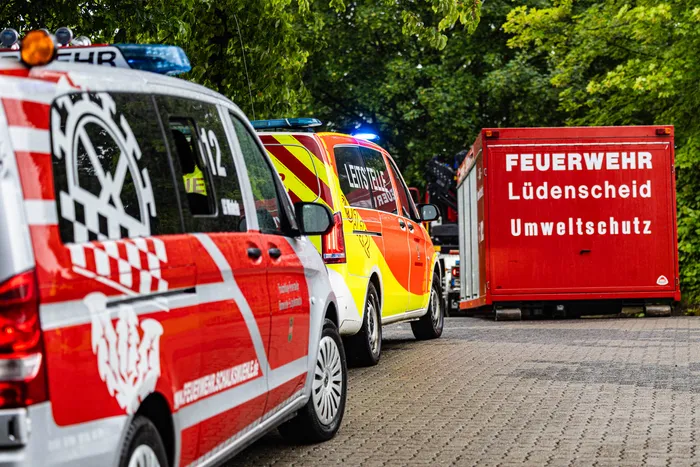 Mehrere rote und gelbe Feuerwehrfahrzeuge stehen auf einer Straße vor Bäumen. Auf einem der Fahrzeuge steht „FEUERWEHR Lüdenscheid Umweltschutz“.