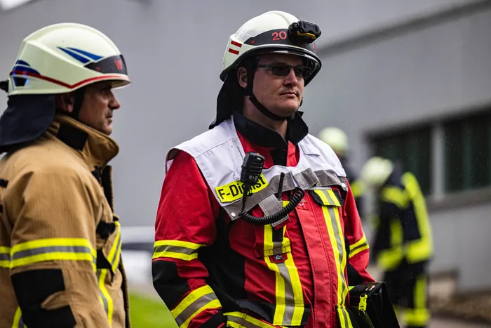 Feuerwehrmann mit Helm und Schutzanzug blickt während eines Gefahrguteinsatzes in Schalksmühle nach vorn. Im Hintergrund sind weitere Einsatzkräfte zu sehen.