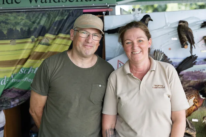 Ein Mann und eine Frau lächeln in die Kamera. Im Hintergrund sind präparierte Vögel und ein Banner mit der Aufschrift „Hegering Lödenscheid“ zu sehen.