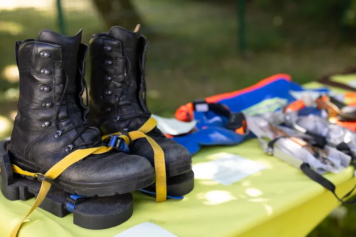 Schwarze, hochgeschnürte Stiefel mit gelben Gurten stehen auf einem hellgrünen Tisch. Daneben liegen ein blaues Tuch und weitere Ausrüstungsgegenstände.