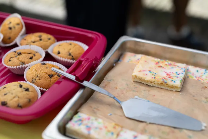 Schokoladenmuffins in Papierförmchen auf einem roten Tablett und mit Streuseln verzierte Kuchenstücke auf einem silbernen Tablett mit Kuchenheber.