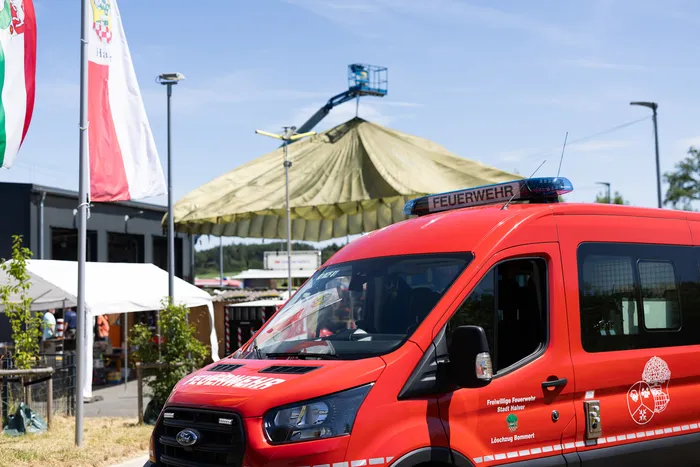 Roter Einsatzwagen der Freiwilligen Feuerwehr Halver mit Aufschrift „FEUERWEHR“ und dem Wappen der Löschgruppe Bommert. Im Hintergrund ein großes Zirkuszelt und eine Flagge.