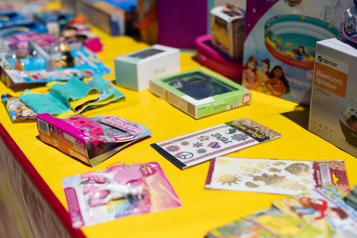 A yellow table is covered with a variety of gifts, including toys, games, and a Bluetooth speaker, likely collected during a celebration.