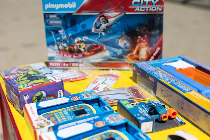 Spielzeugautos und Playmobil-Sets stehen auf einem Tisch, darunter ein Spielzeug-Polizeiauto und ein Hubschrauber auf der Verpackung eines Playmobil City Action Sets.