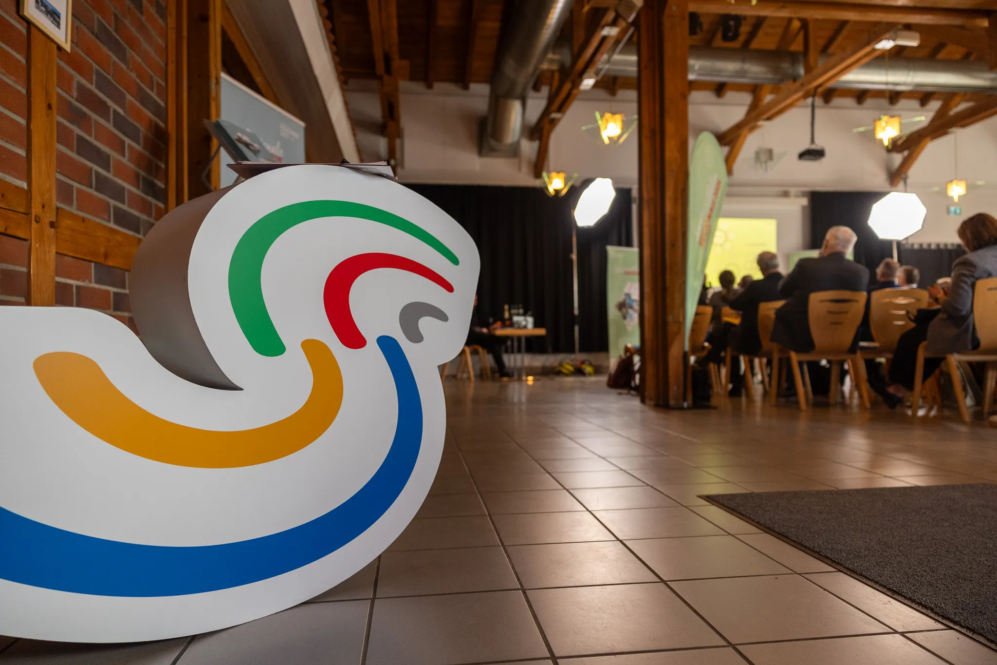 Bunte, geschwungene Skulptur im Vordergrund, im Hintergrund Menschen auf Stühlen in einem hellen Raum während der Konferenz „Vielfalt Wohnen und Arbeiten“.