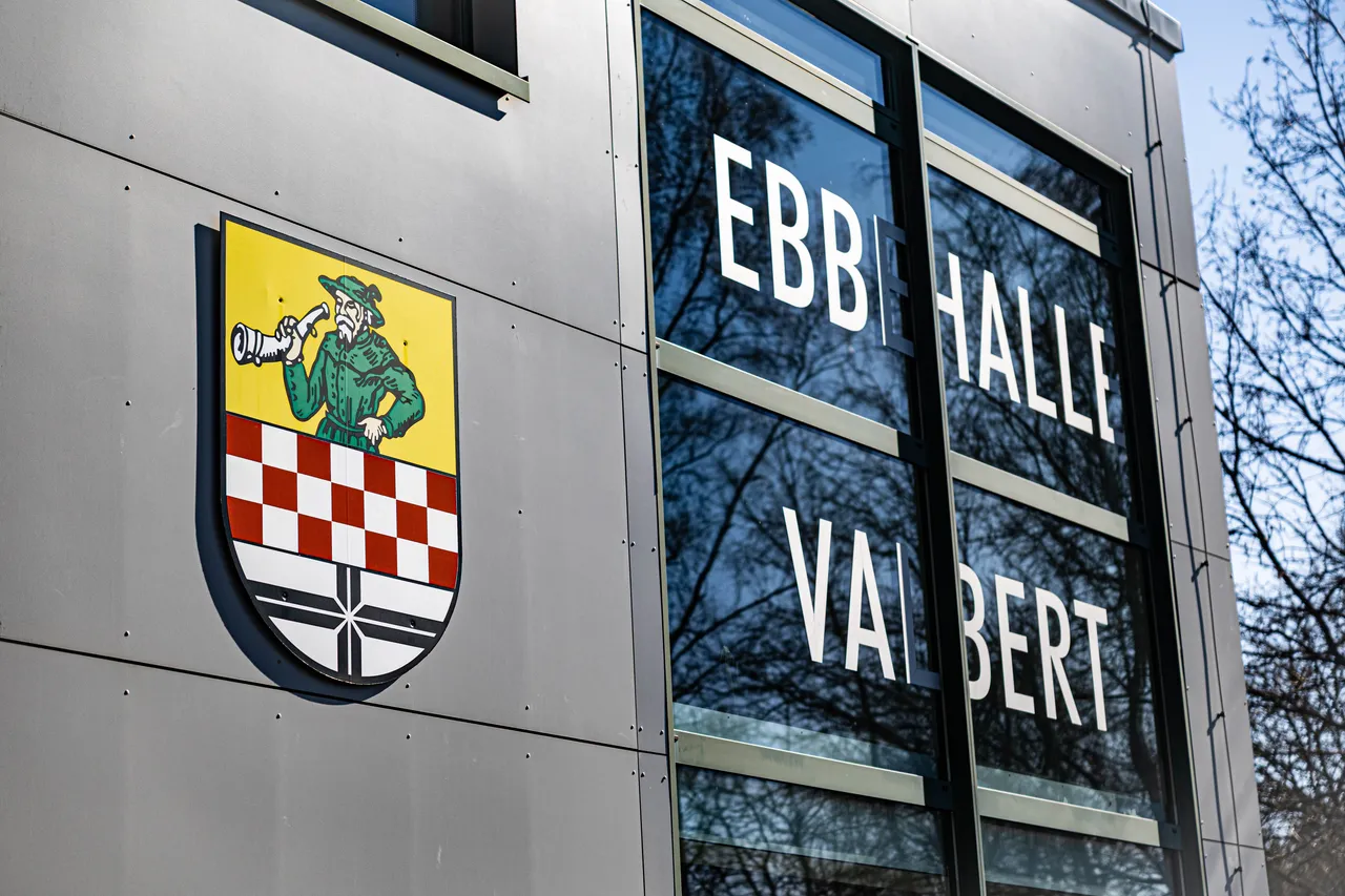 Das Wappen von Valbert links neben dem Schriftzug „Ebb Halle Valbert“ an der Fassade eines modernen Gebäudes.