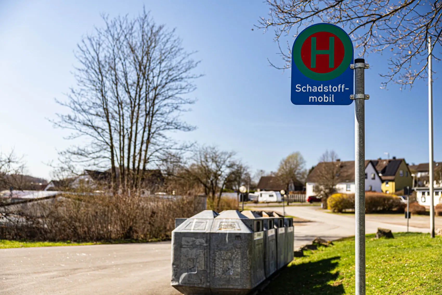 Schild „Schadstoffmobil“ mit rotem H auf grünem Grund an einer Haltestelle mit Containern für Gefahrstoffe in Meinerzhagen-Valbert.