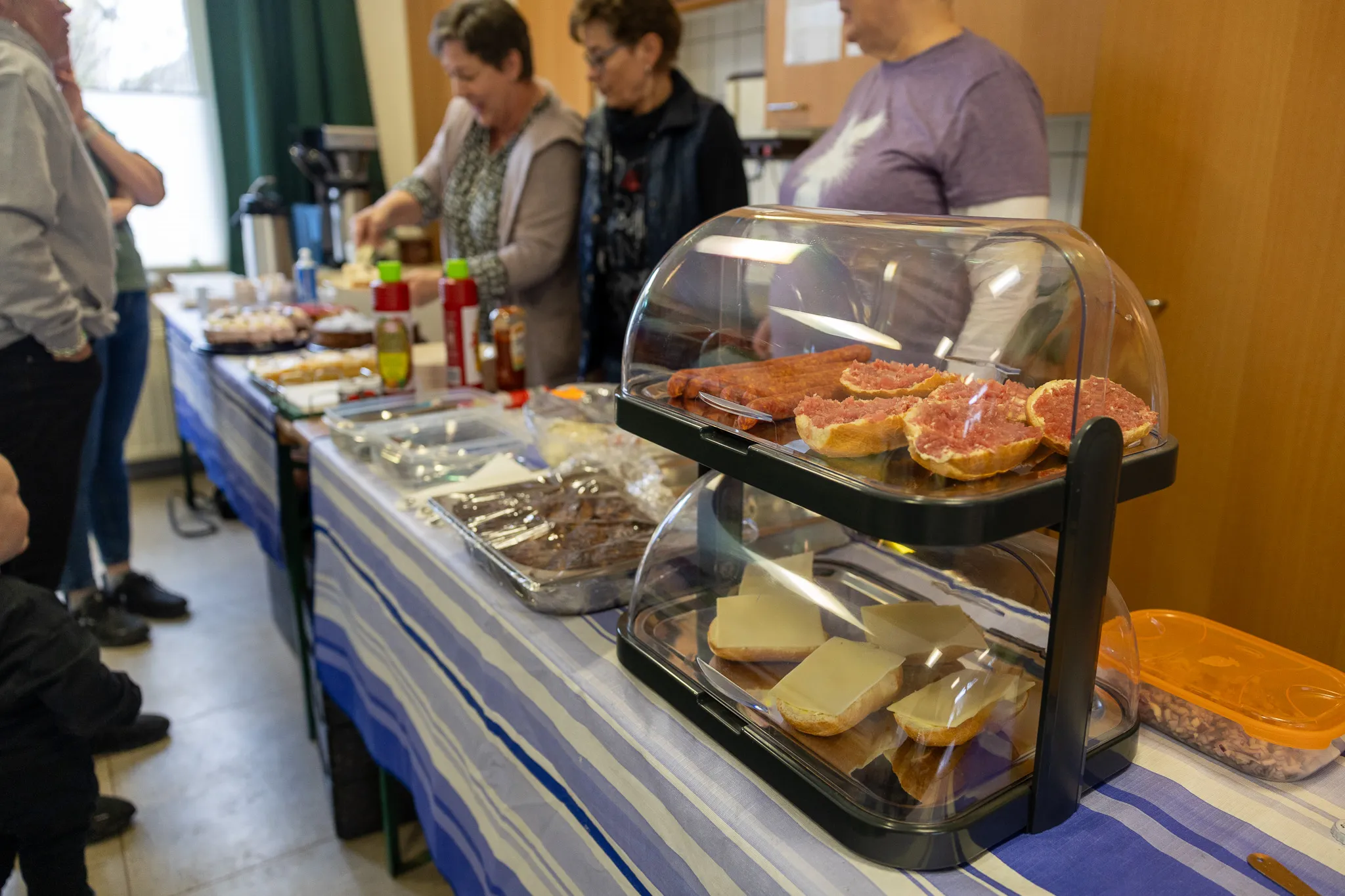 Blick auf einen Tisch mit belegten Broten und Gebäck, im Hintergrund stehen Menschen während des Ostereierschießens der Hülscheider Schützen.