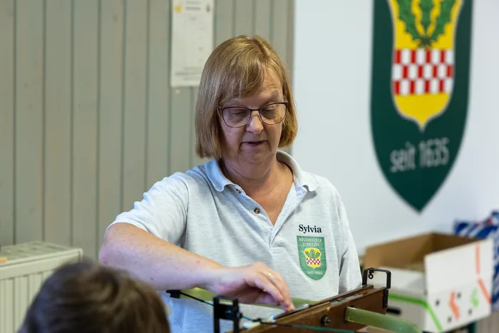 Eine Frau mit Brille und rotem Poloshirt arbeitet konzentriert an einer Maschine, vermutlich im Zusammenhang mit dem Ostereierschießen der Hülscheider Schützen.
