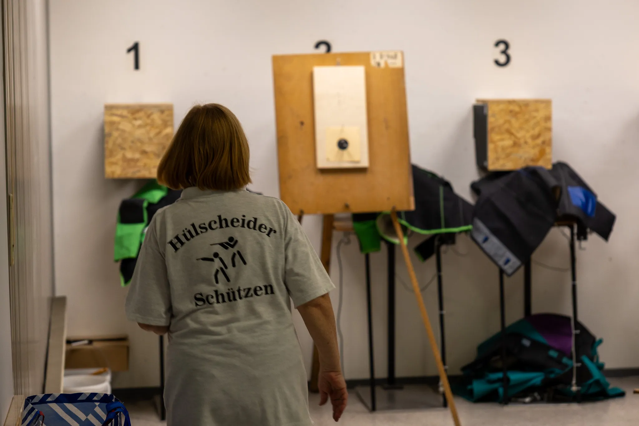 Eine Frau steht mit dem Rücken zum Betrachter in einer Schießanlage, vor ihr drei Zielscheiben mit Einschusslöchern.