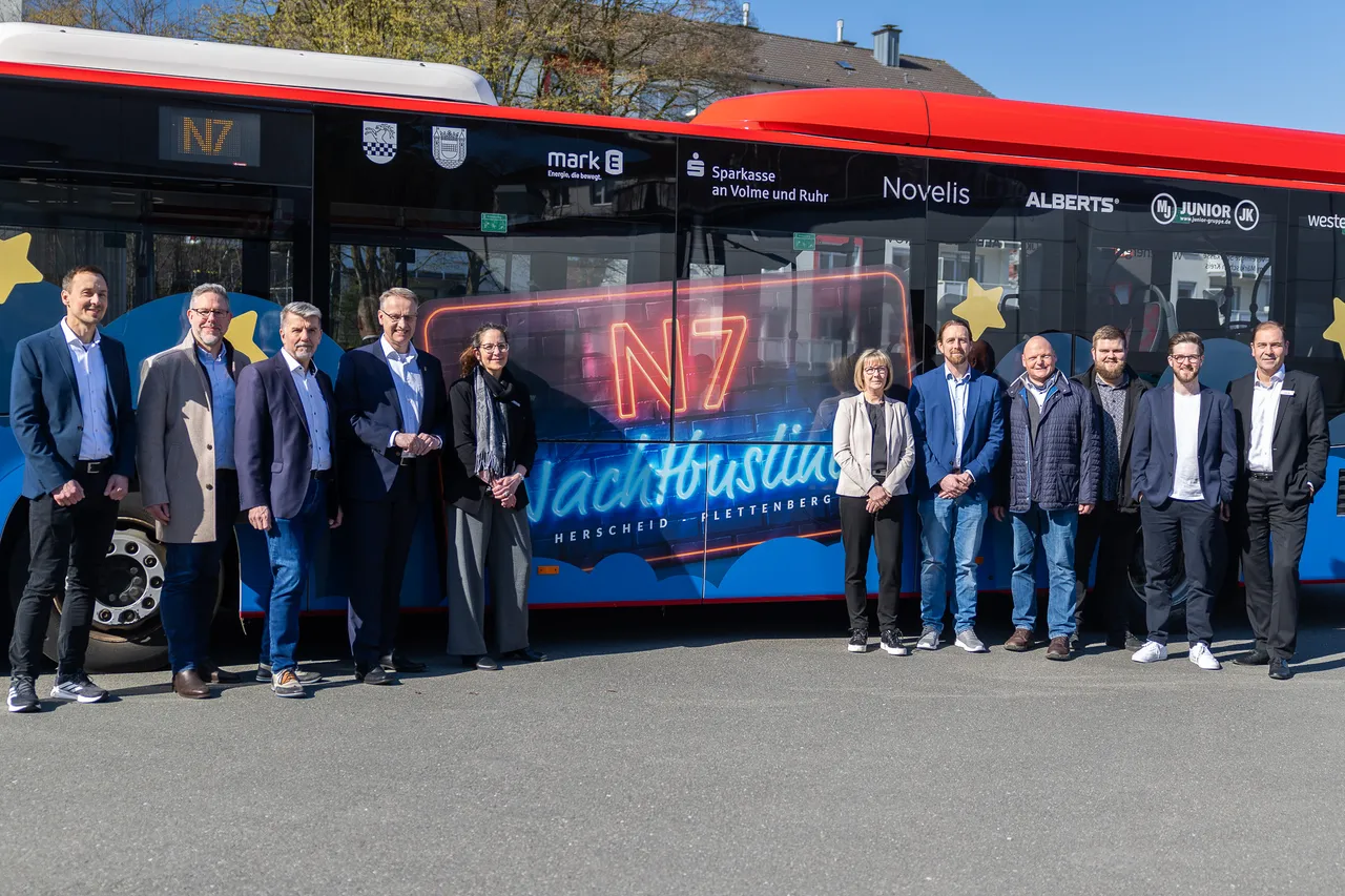 Gruppe von Personen steht vor einem roten Bus mit der Aufschrift „N7 Nachtbus Herscheid – Plettenberg“ und Sponsorenlogos.