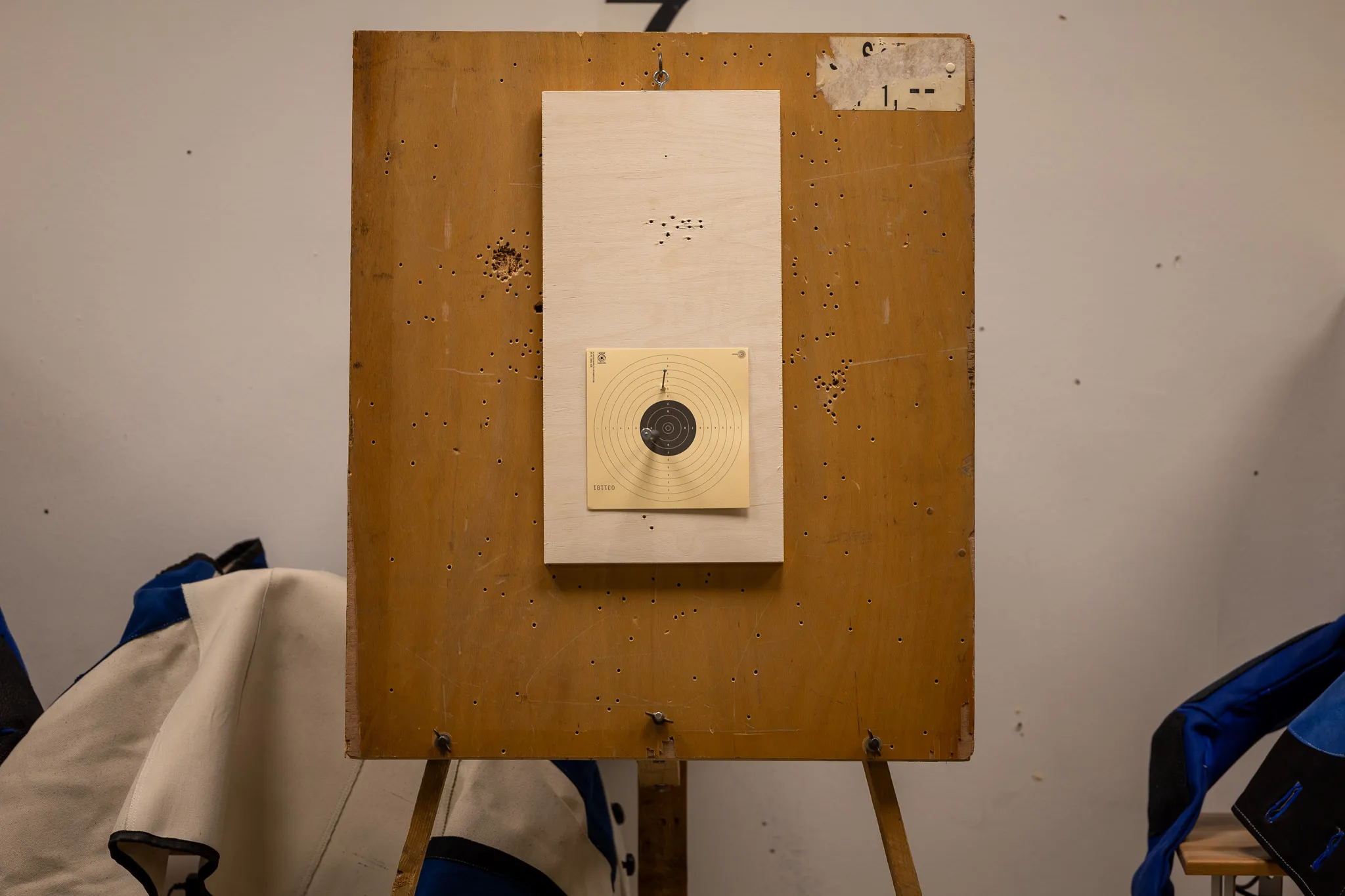 Skeet-Ziel auf einer Holzplatte mit zahlreichen Einschusslöchern, umgeben von blauen und weißen Jacken.