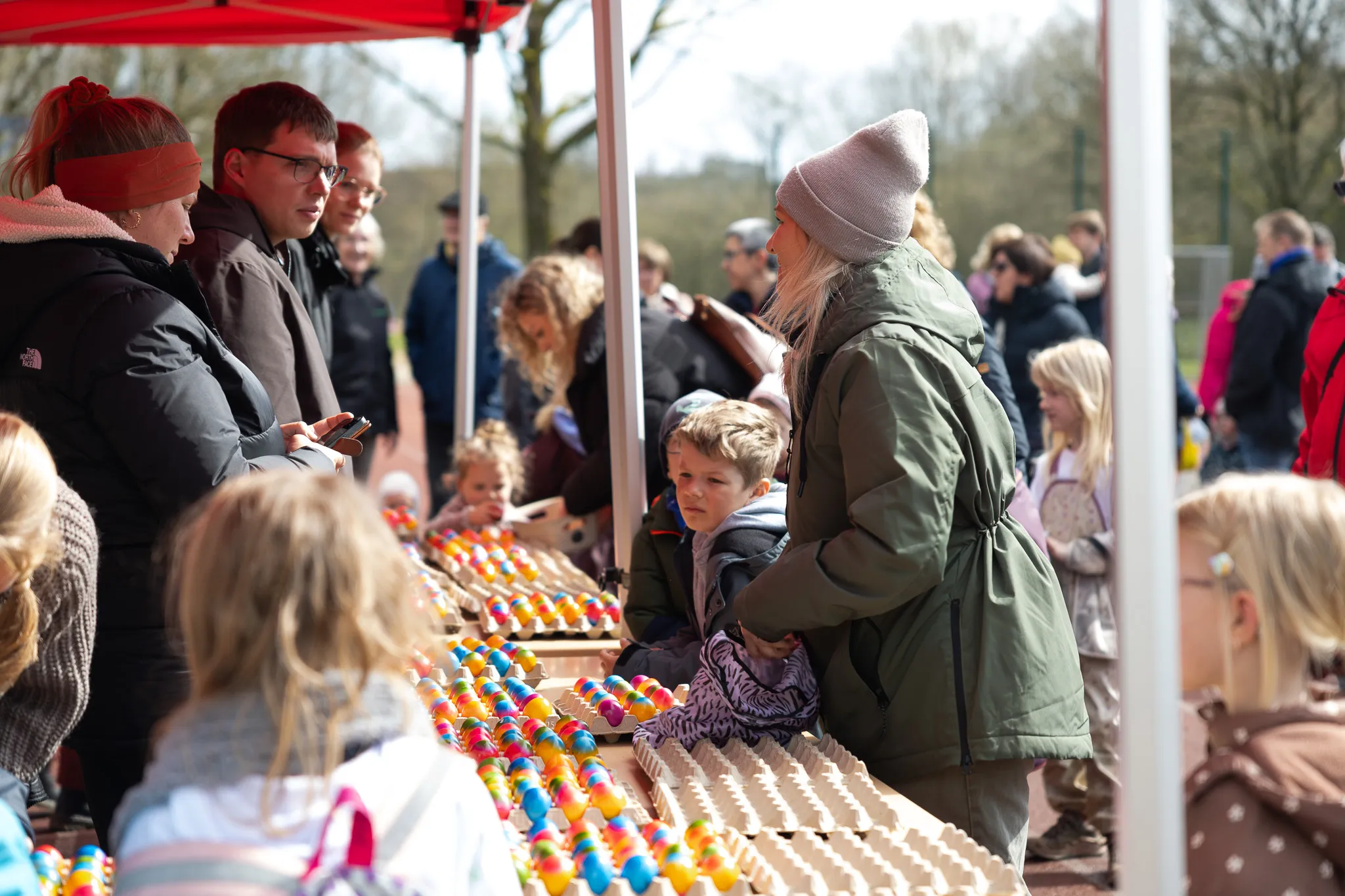 Familien stehen an einem Tisch mit bunten Ostereiern während einer Ostereiersuche im Freien.