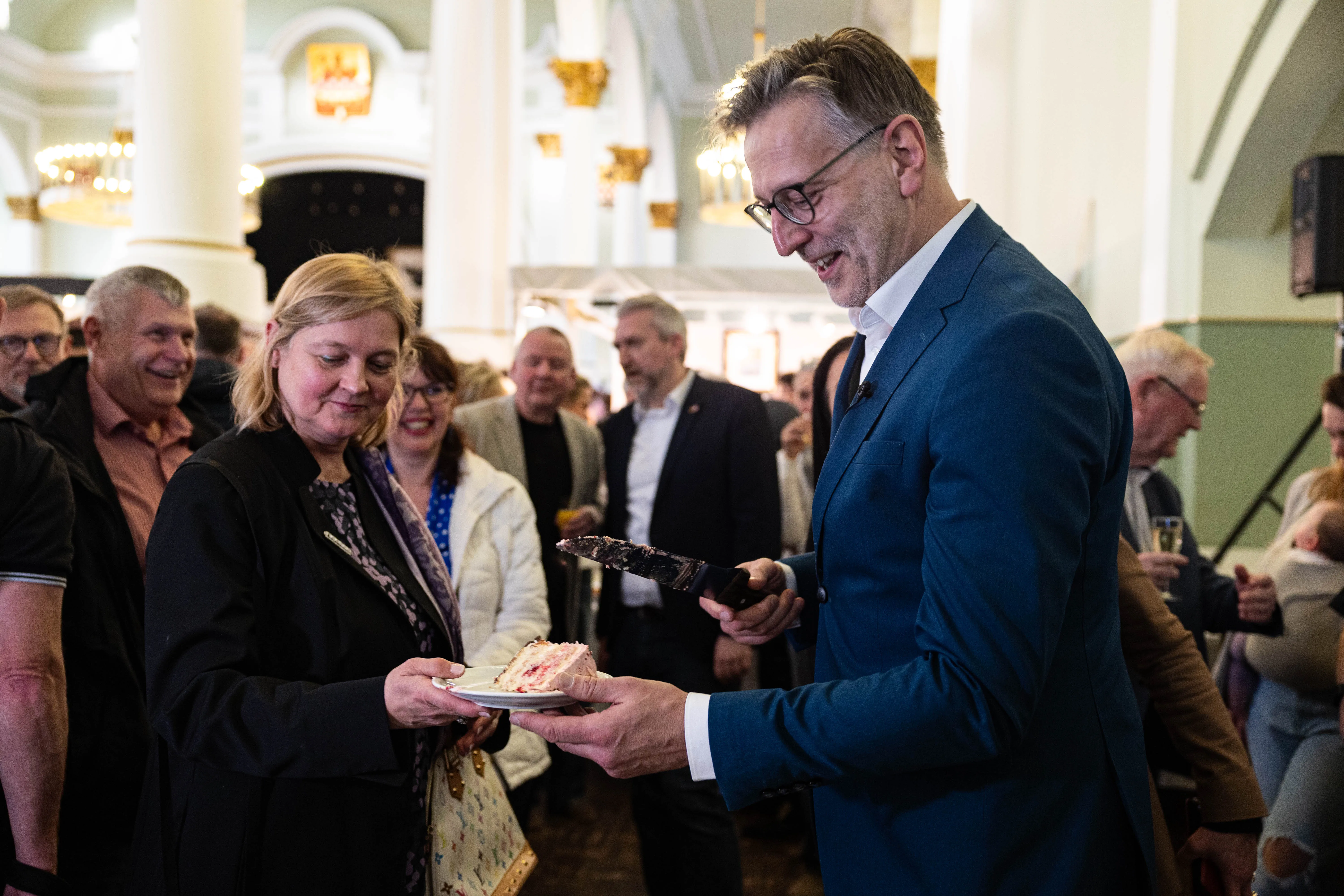 Detlev Kümmel, der Organisator der Messe, erhält ein Stück Geburtstagstorte von einer Frau während der Vernissage in Lüdenscheid.