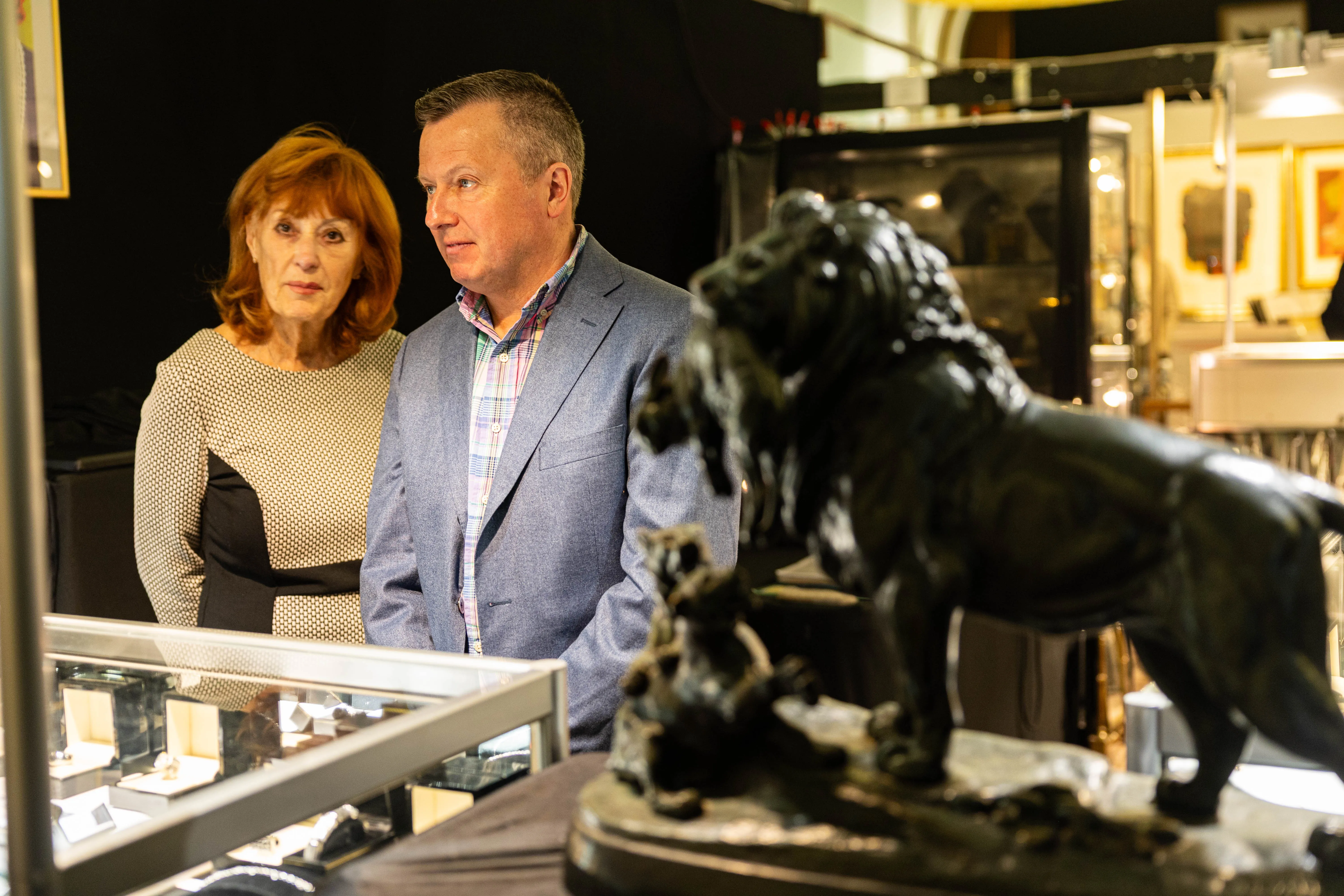 Zwei Personen betrachten eine bronzene Löwenfigur in einer Vitrine auf einer Kunstmesse.
