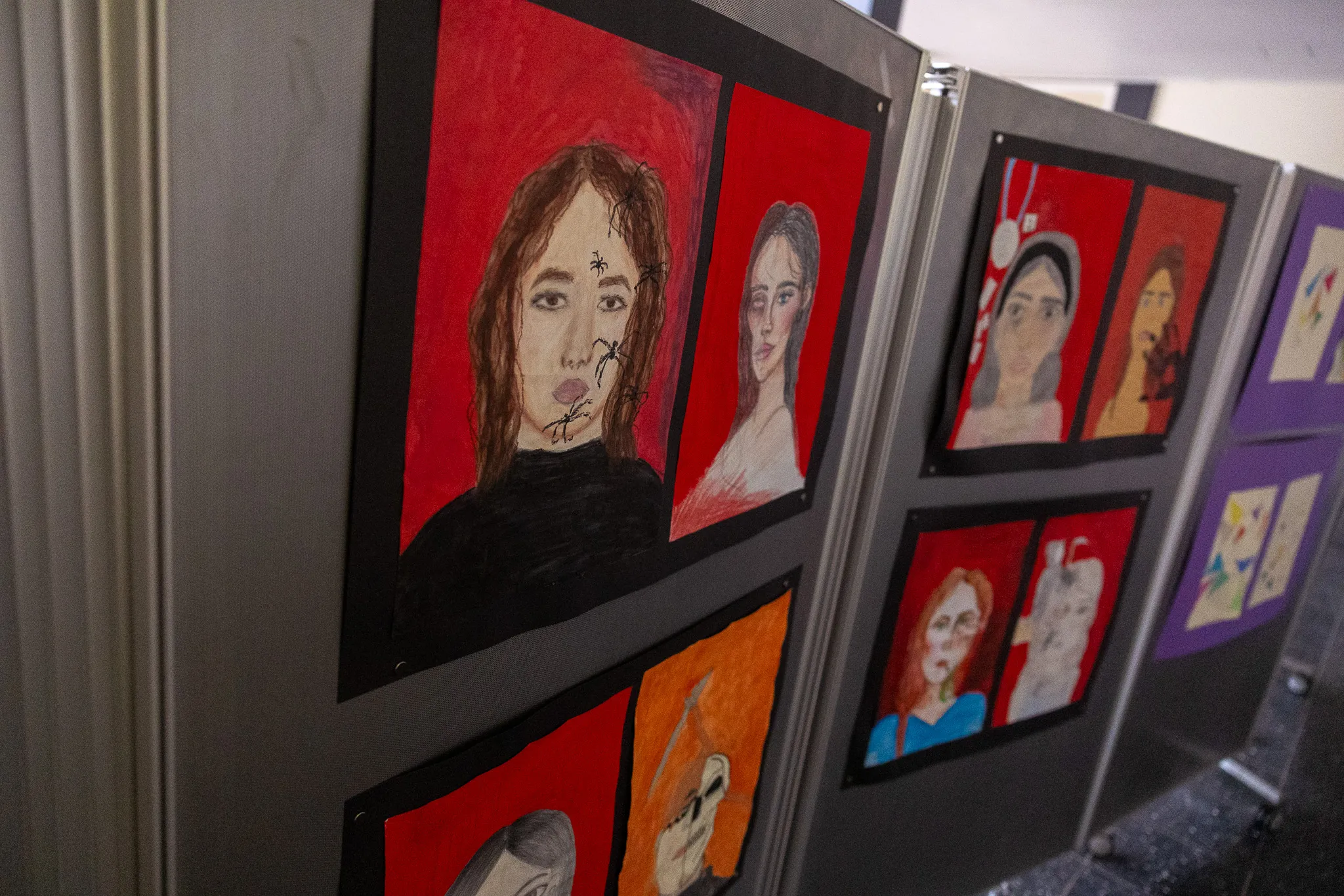 Mehrere Porträts, gemalt in leuchtenden Farben, hängen an einer grauen Wand in einer Galerieausstellung von Schülerarbeiten.