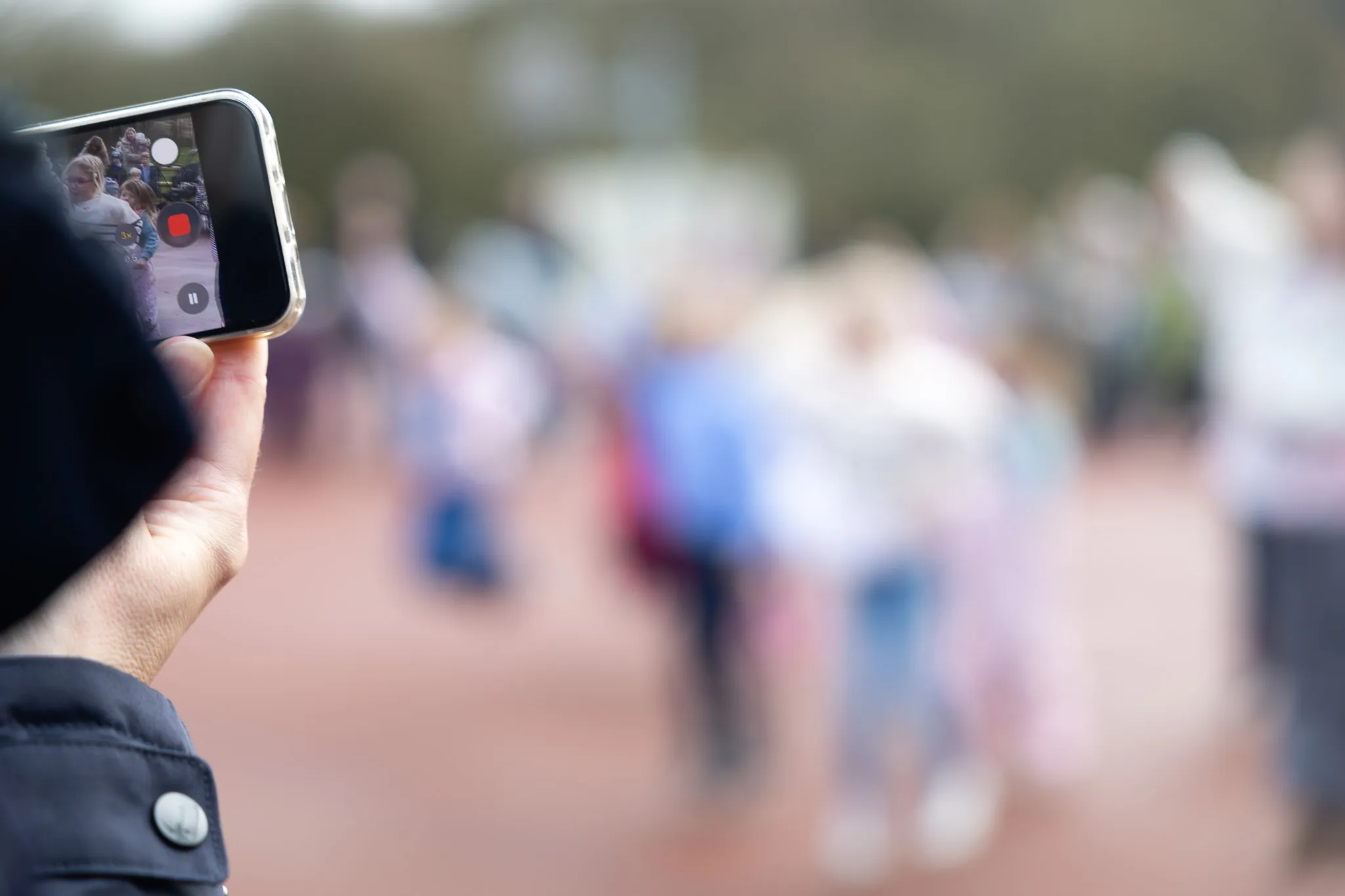 Hand hält Smartphone, das eine Gruppe Kinder bei einer Ostereiersuche filmt.