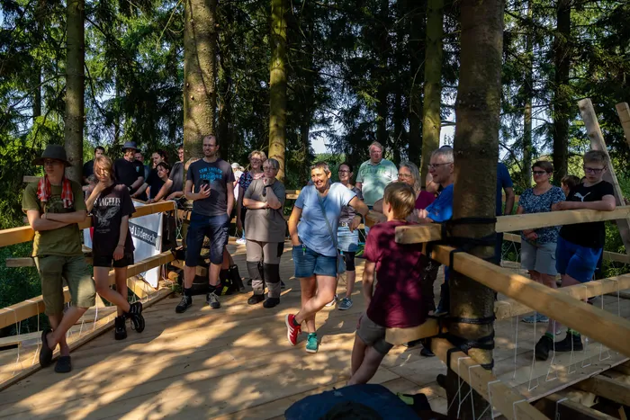 Eine Gruppe von Jugendlichen steht auf der hölzernen Plattform eines Baumhauses im Wald.