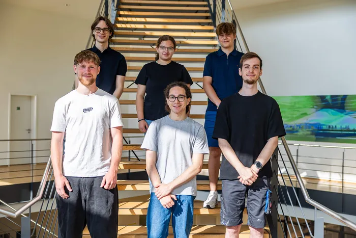 Sechs neue Auszubildende des Unternehmens Werner Turck posieren auf einer Holztreppe in einem hellen Gebäude.