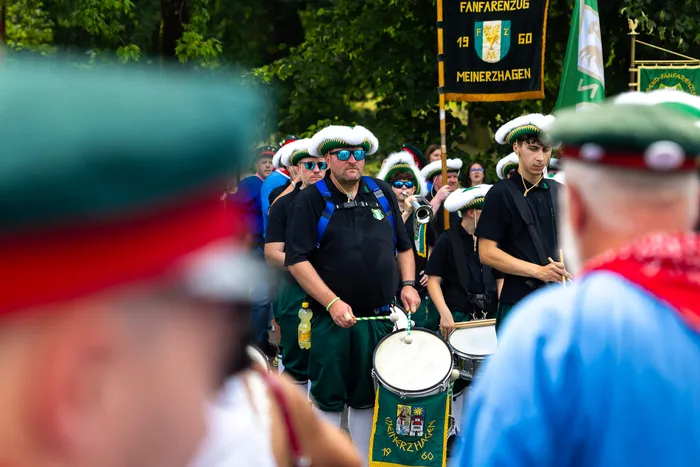Mitglieder der Meinerzhagener Schützengilde in einheitlicher Kleidung ziehen in einer Parade durch die Straßen, ein Mann spielt dabei eine Trommel.