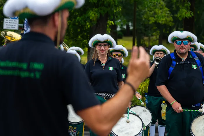 Mitglieder der Meinerzhagener Schützengilde in schwarzen Poloshirts und weißen, flauschigen Hüten stehen mit Trommeln im Freien.