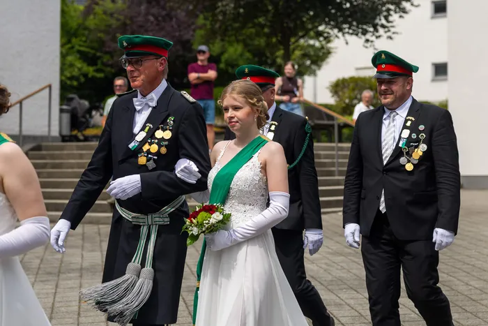 Stefan Schneider in schwarzer Uniform mit Orden und grüner Mütze geht mit einer jungen Frau in weißem Kleid und grüner Schärpe.