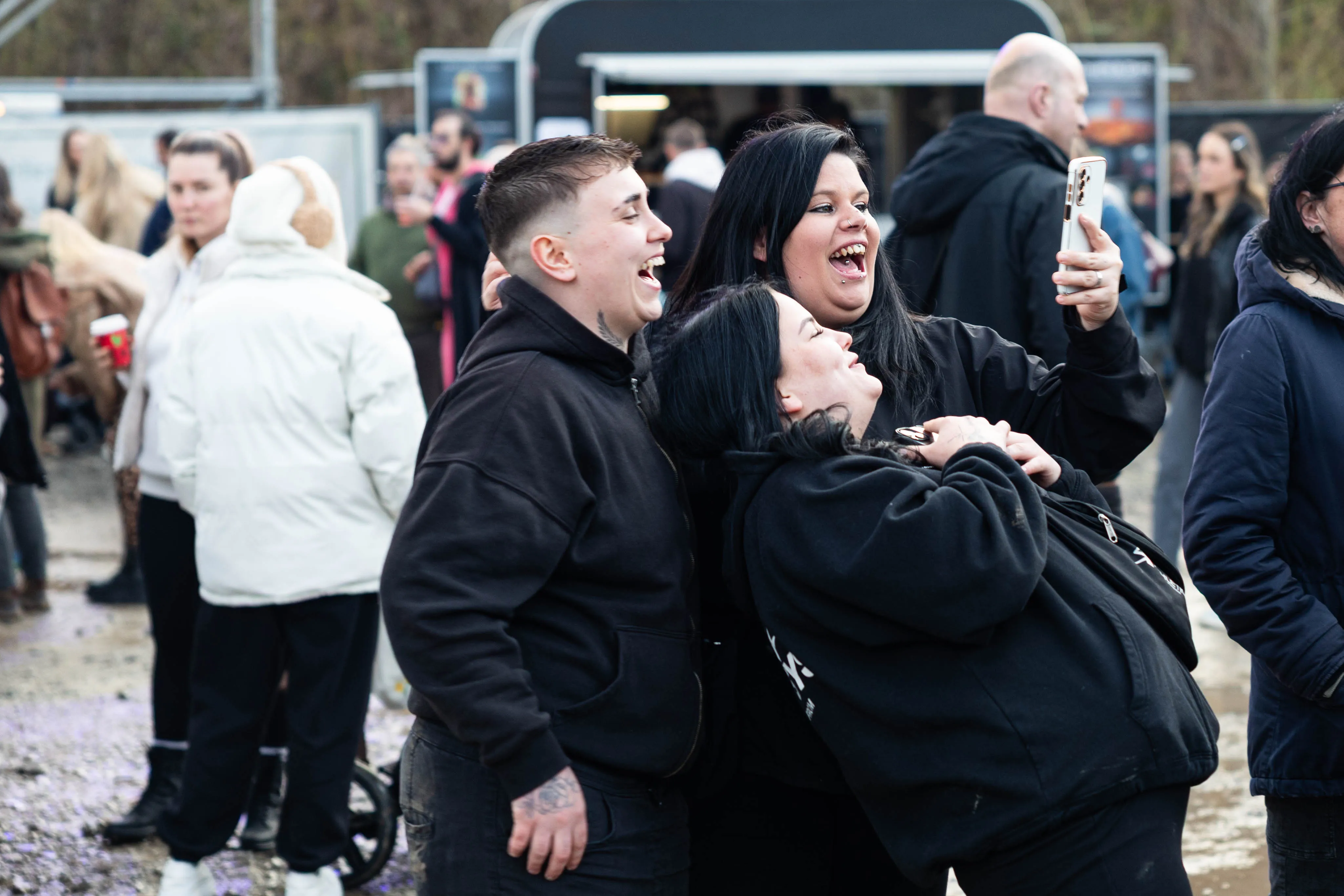 Drei junge Frauen umarmen sich ausgelassen und machen ein Selfie auf dem Gelände des Osterfeuers „Burn the Fox“ in Lüdenscheid.
