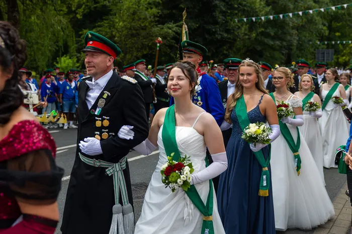 Stefan Schneider in schwarzer Uniform geht arm in arm mit einer jungen Frau in weißem Kleid bei einer Prozession der Meinerzhagener Schützengilde.