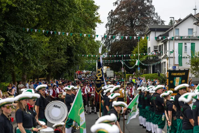 Mitglieder der Schützengilde in grünen Uniformen ziehen mit Musikinstrumenten und einem Banner durch eine Straße.