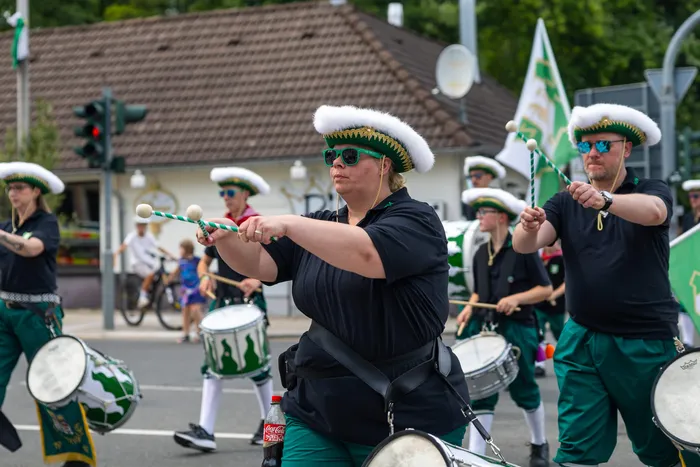 Mitglieder einer Marschkapelle in schwarz-grünen Uniformen und weißen Hüten spielen Trommeln bei einem Umzug.