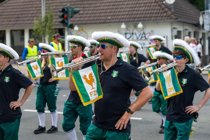 Mitglieder der Meinerzhagener Schützengilde in schwarzen Poloshirts, grünen Hosen und weißen Federhüten spielen Trompeten.